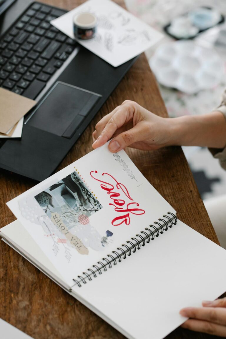 Close-up of a person holding an inspirational notebook next to a laptop on a wooden desk.